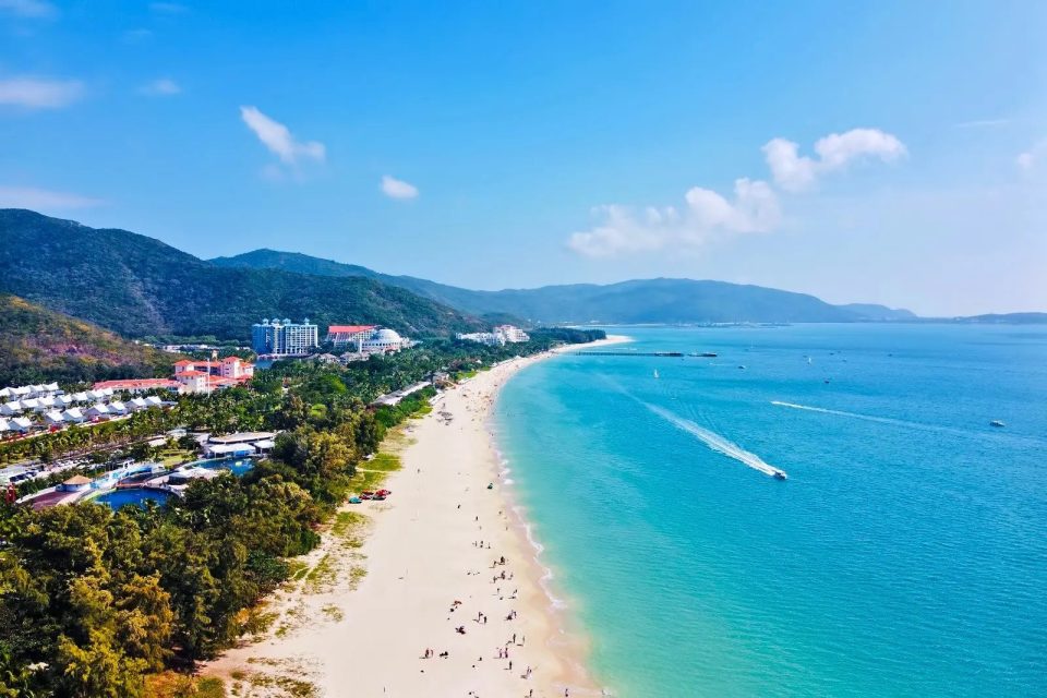 Yalong Bay beach with its pristine white sand and clear blue water, lined with palm trees.