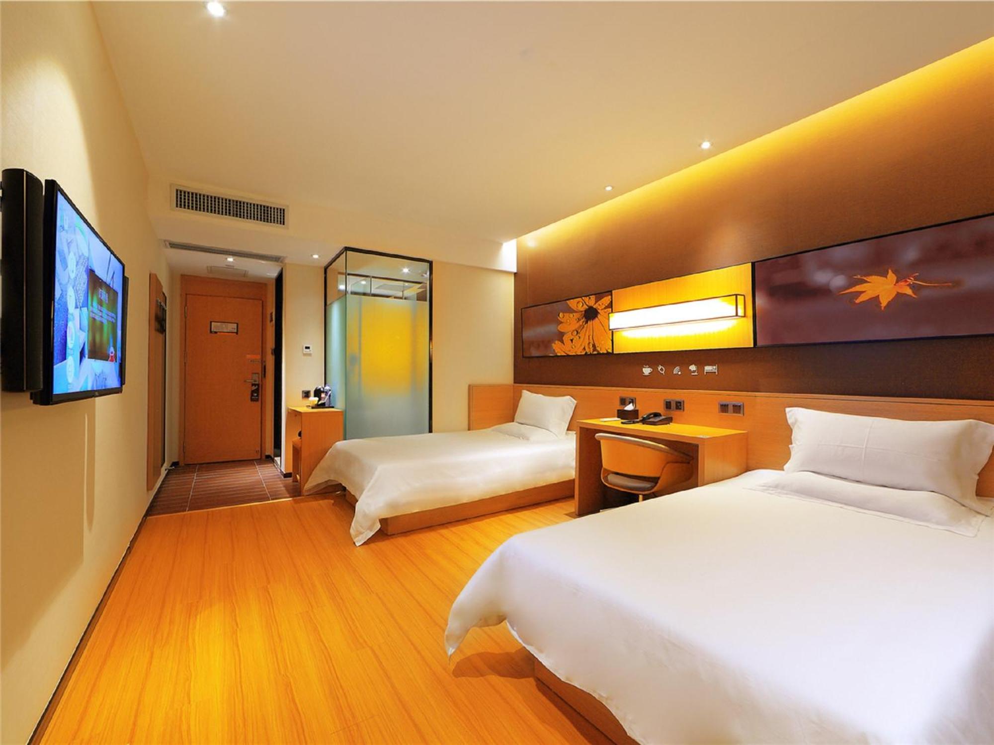 A hotel room with two single beds, a desk, and a television.