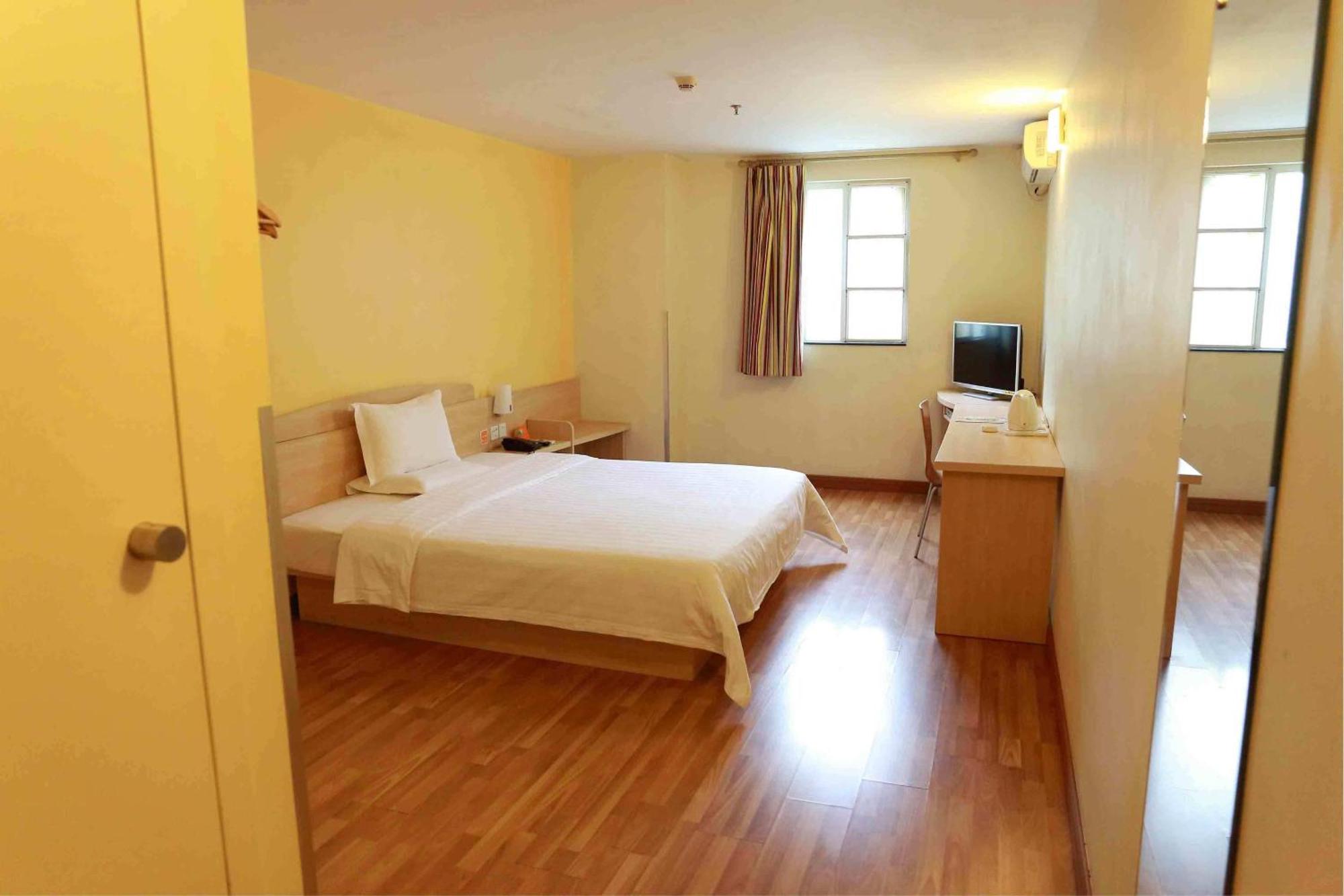 A basic hotel room with a double bed, a small desk, and a window.